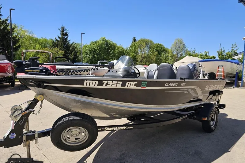Slide: The Image of 2014 Alumacraft Classic 165 boat on trailer, parked outdoors on a sunny day. - 14