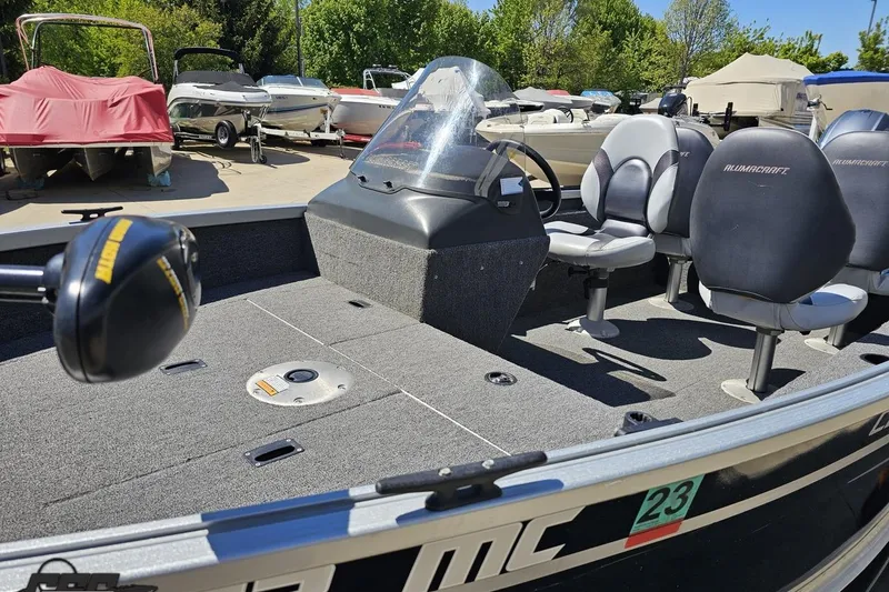 Slide: The Image of 2014 Alumacraft Classic 165 boat interior with seating and steering console, parked among other boats. - 15