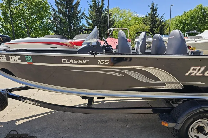 Slide: The Image of 2014 Alumacraft Classic 165 boat on trailer, parked outdoors with trees in background. - 20