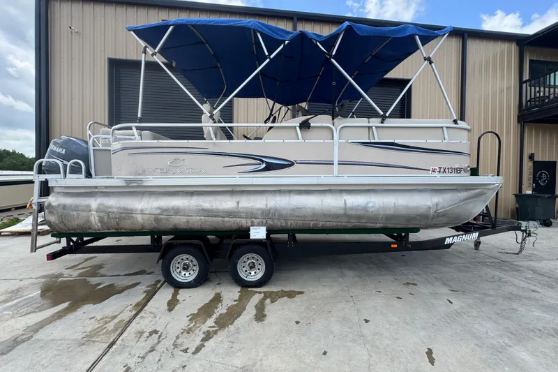 The Image of 2011 Veranda Tritoon boat on trailer with blue canopy, parked outside a building. - 1