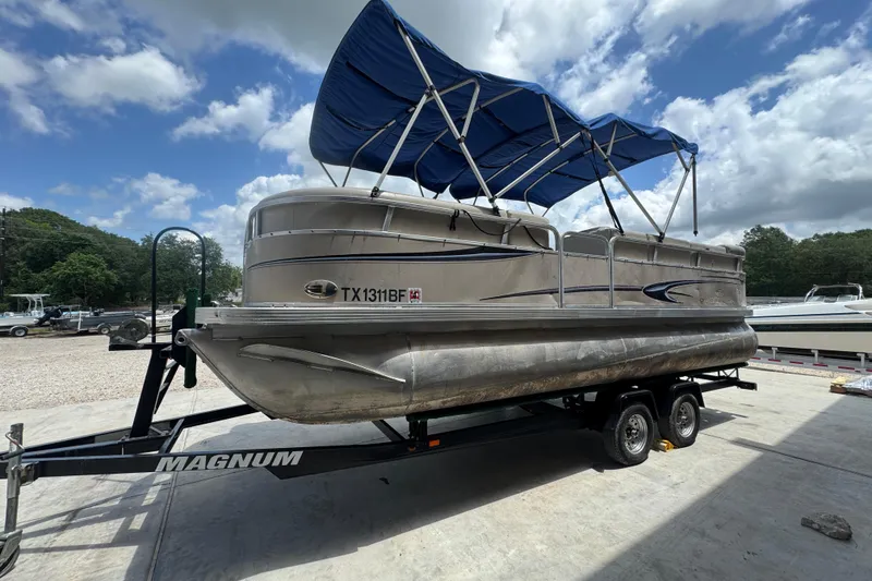Slide: The Image of 2011 Veranda Tritoon boat on trailer with blue canopy, parked outdoors under cloudy sky. - 3