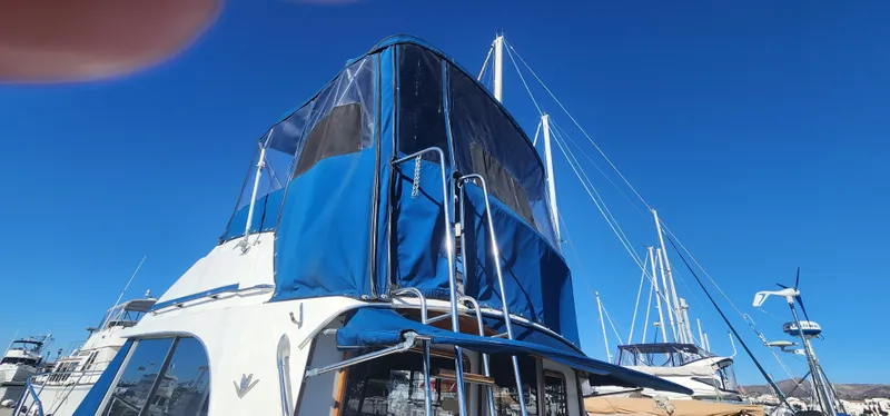 Slide: The Image of 1985 Bertram 33 Flybridge Cruiser with blue canopy, docked under clear blue sky. - 1