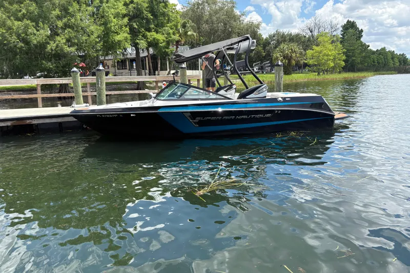 The Image of 2014 Nautique Super Air Nautique 210 boat docked on a serene lake. - 0