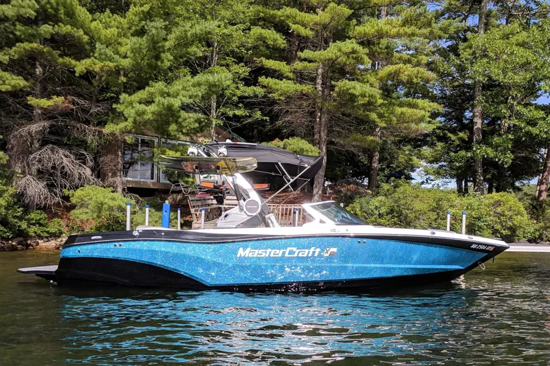 The Image of 2018 MasterCraft XT23 boat on a lake, surrounded by lush trees. - 0