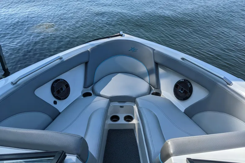 Slide: The Image of 2018 MasterCraft XT23 boat interior with gray seating and speakers, on calm water. - 2