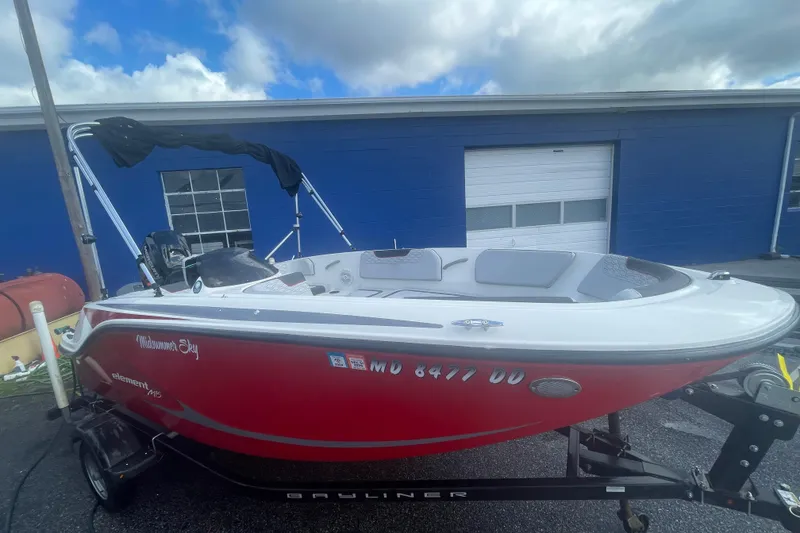 Slide: The Image of 2022 Bayliner Element M15 boat in red, parked outdoors near a blue building. - 1