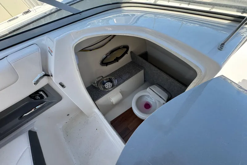 Slide: The Image of Interior of 2018 Chaparral 250 Suncoast boat featuring a compact marine toilet. - 17