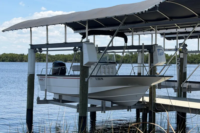 The Image of 2012 Boston Whaler 190 Montauk boat on lift by serene lake with canopy. - 1