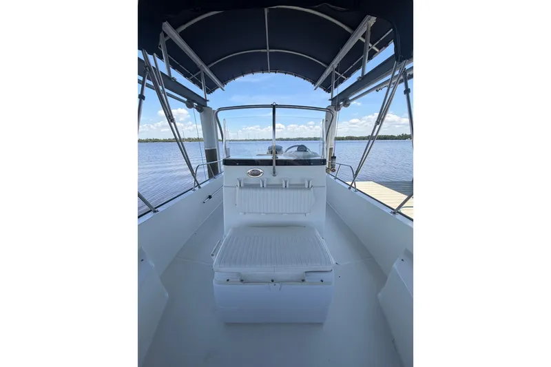 Slide: The Image of 2012 Boston Whaler 190 Montauk boat interior with canopy, docked on a calm lake. - 8