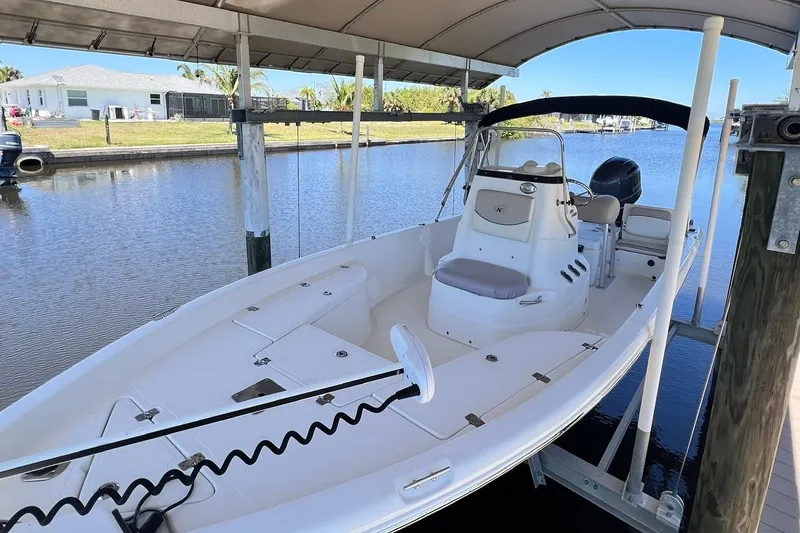 The Image of 2016 NauticStar 2110 Sport boat docked under a canopy on a calm waterway. - 0