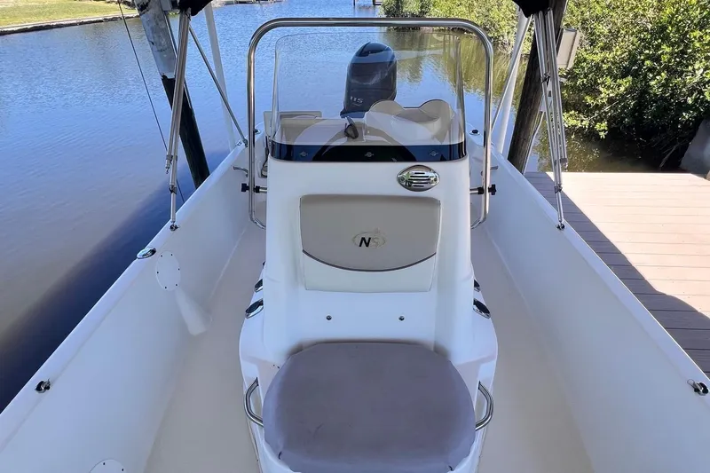 Slide: The Image of 2016 NauticStar 2110 Sport boat interior with steering console, docked by a calm waterway. - 3