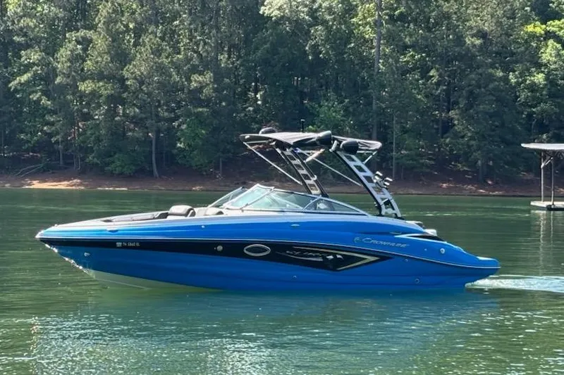 The Image of 2022 Crownline 265 SS SURF boat on a serene lake with forest backdrop. - 0