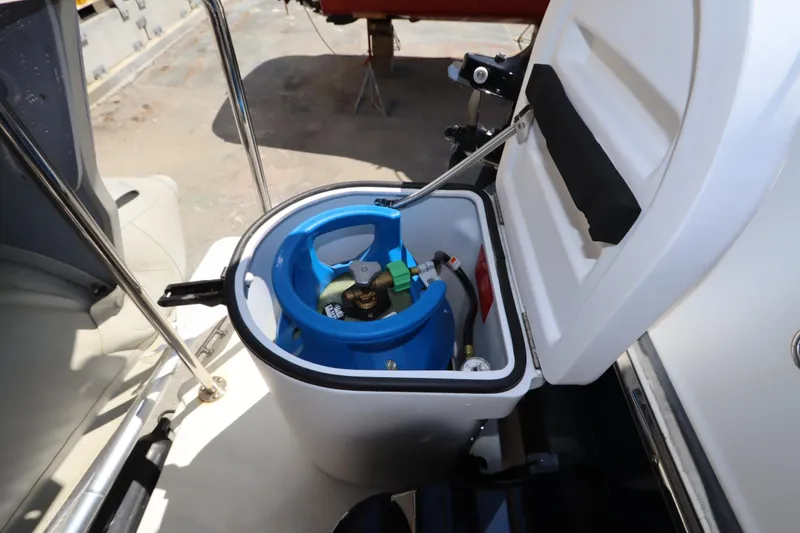 Slide: The Image of Open storage compartment on 2015 Ranger Tugs R-27 boat, revealing a blue propane tank. - 16