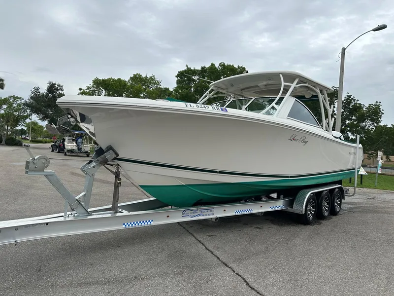 Slide: The Image of 2018 Sailfish 325 DC boat on trailer, parked outdoors under cloudy sky. - 2