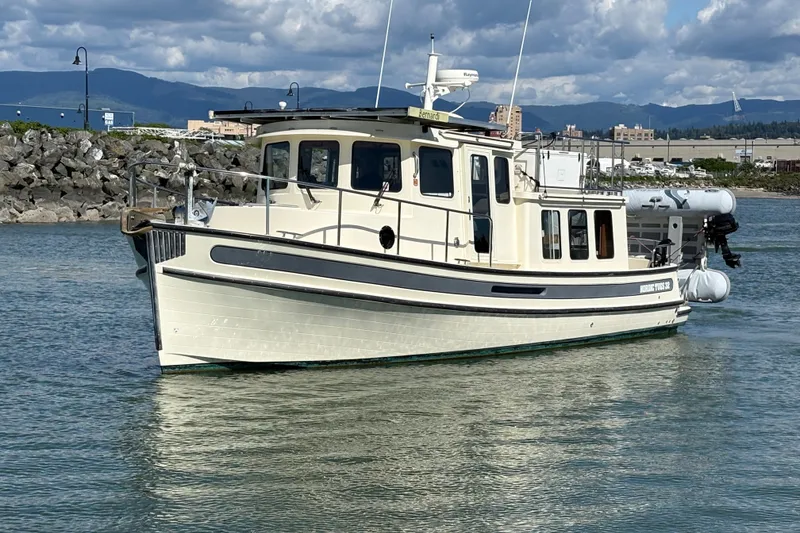 Slide: The Image of 2004 Nordic Tug 32 cruising in a scenic harbor with rocky shoreline and mountains. - 1
