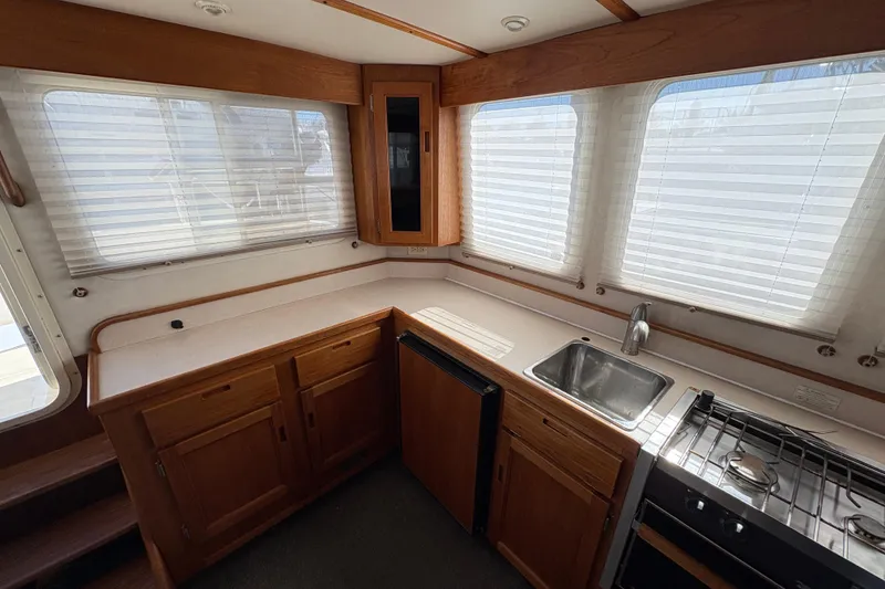 Slide: The Image of Interior of a 2004 Nordic Tug 32, featuring a compact kitchen with wood cabinetry. - 20