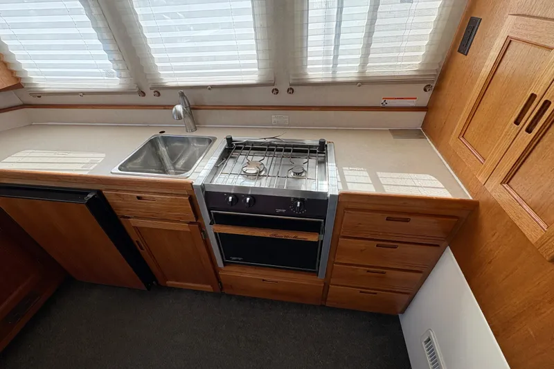 Slide: The Image of Compact kitchen in a 2004 Nordic Tug 32 boat with stove, sink, and wooden cabinetry. - 22