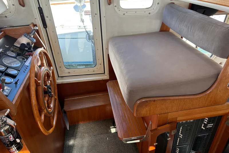 Slide: The Image of 2004 Nordic Tug 32 interior helm with wooden steering wheel and cushioned seating. - 25