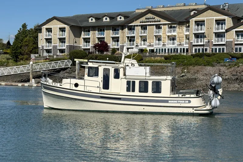Slide: The Image of 2004 Nordic Tug 32 cruising near a waterfront hotel, showcasing classic design and serene waters. - 3
