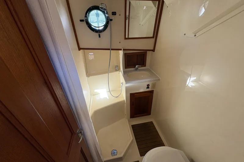 Slide: The Image of Bathroom interior of a 2004 Nordic Tug 32, featuring a shower, sink, and porthole window. - 34
