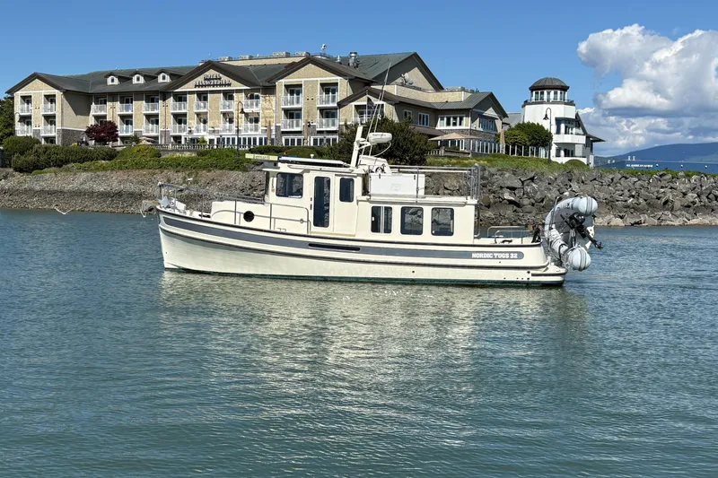 Slide: The Image of 2004 Nordic Tug 32 boat on water near a hotel and lighthouse. - 4