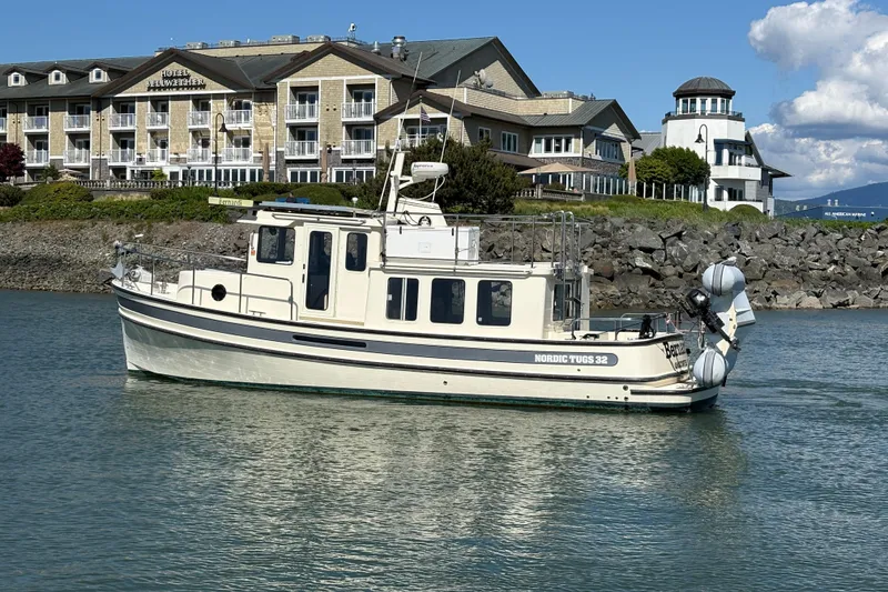 Slide: The Image of 2004 Nordic Tug 32 boat on water near a hotel and rocky shoreline. - 5