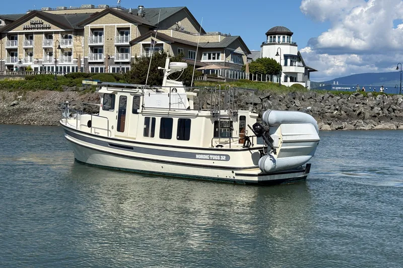 Slide: The Image of Nordic Tug 32 boat from 2004 on water near a hotel and rocky shoreline. - 6