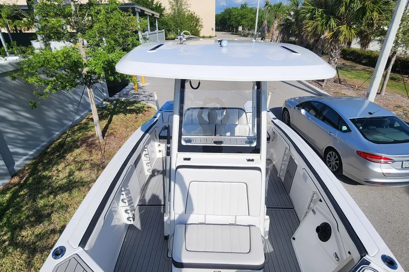 Slide: The Image of 2022 Yamaha 255 FSH Sport E boat with sleek design, parked near trees and a car. - 34