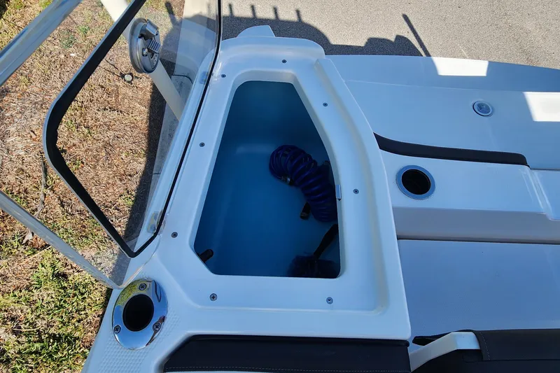 Slide: The Image of Open storage compartment on a 2022 Yamaha 255 FSH Sport E boat, featuring a coiled hose. - 8