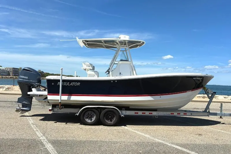 The Image of 2019 Regulator 23 boat on trailer by the waterfront under a clear blue sky. - 0