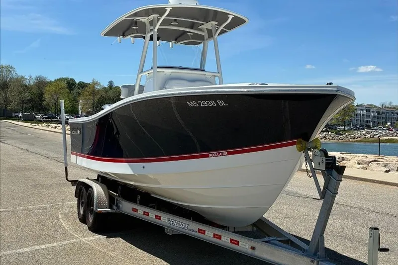 Slide: The Image of 2019 Regulator 23 boat on trailer, parked near waterfront under clear blue sky. - 1