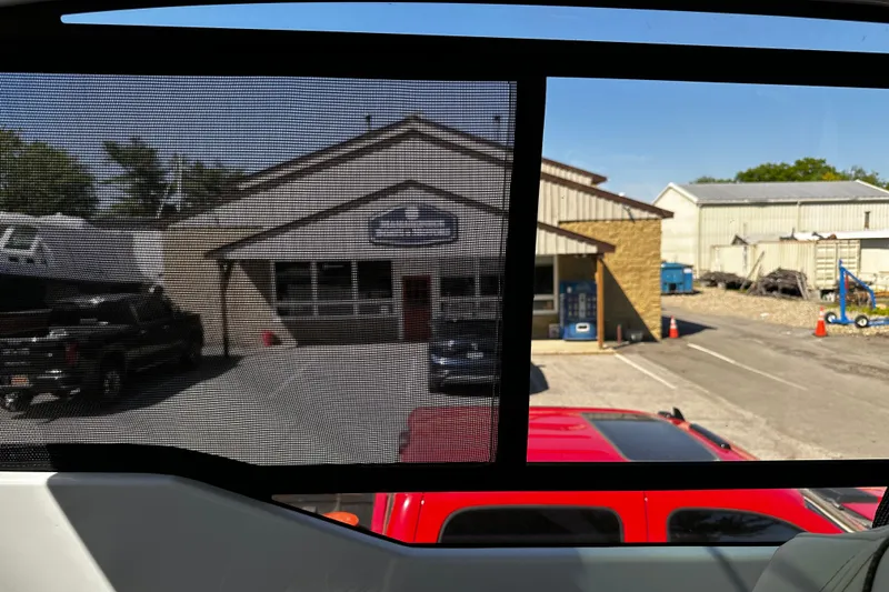 Slide: The Image of View through a window screen showing a building and parked vehicles outside. - 25