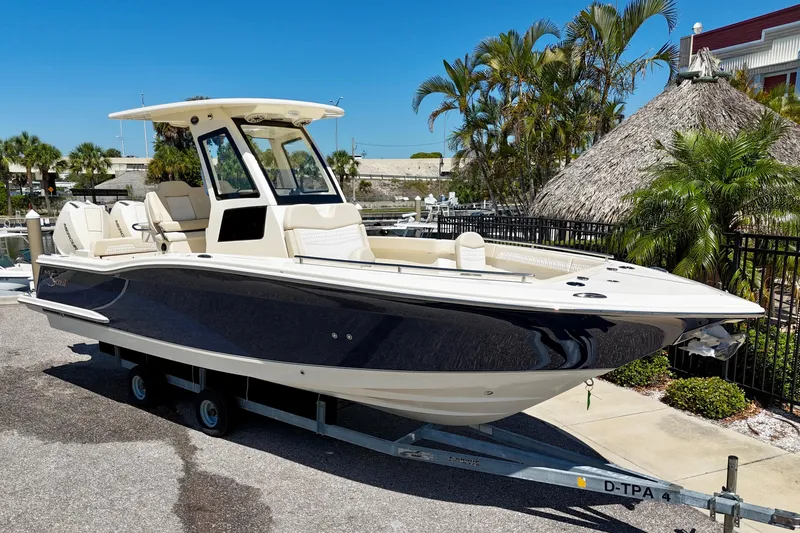 The Image of 2026 Scout 260 LXF boat on trailer, parked near tropical foliage. - 0