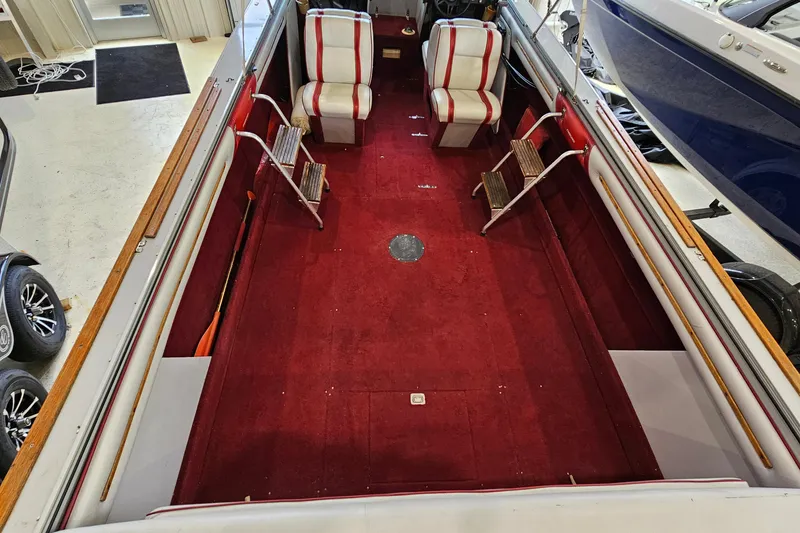 Slide: The Image of 1988 Crestliner 2281 boat interior with red carpet and striped seats in a showroom. - 7