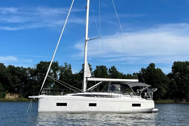 The Image of 2022 Bavaria C38 sailboat on calm water, surrounded by trees under a clear blue sky. - 0
