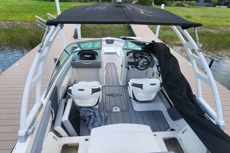 Slide: The Image of 2022 Chaparral 21 SSi OB boat interior with seating and steering wheel, docked by a wooden pier. - 54
