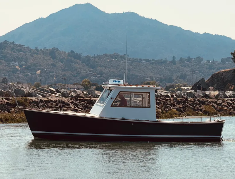 Slide: The Image of 1974 Dyer 29' Sport Fisher boat on calm water with mountainous backdrop. - 5