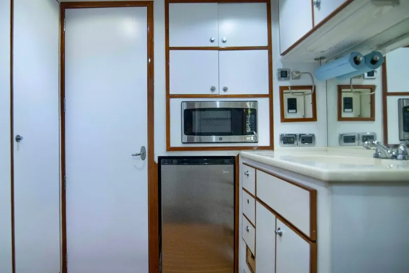 Slide: The Image of Compact yacht kitchen with white cabinetry, microwave, and sink, aboard a 2001 Hargrave 94 model. - 90