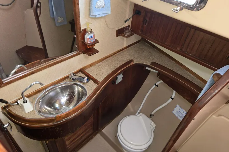 Slide: The Image of 1989 Island Packet 35 yacht bathroom with wooden cabinetry, stainless steel sink, and marine toilet. - 10