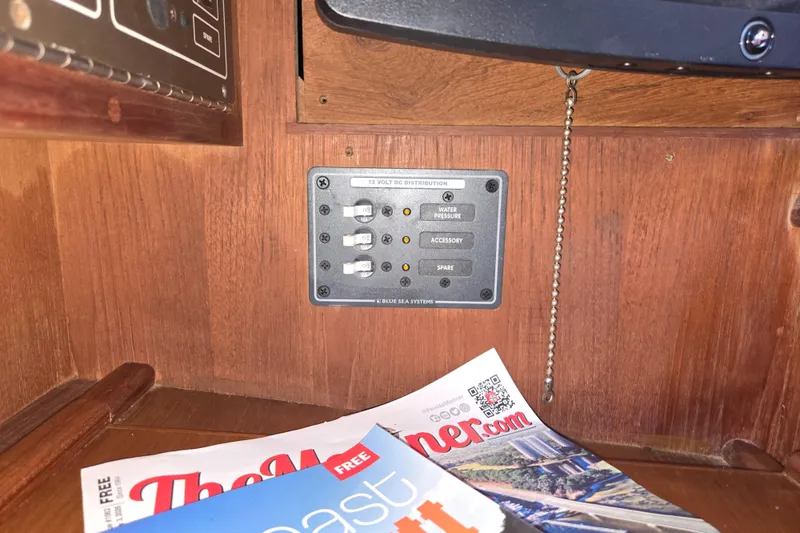 Slide: The Image of Electrical panel inside 1989 Island Packet 35 sailboat with magazines on wooden surface. - 39