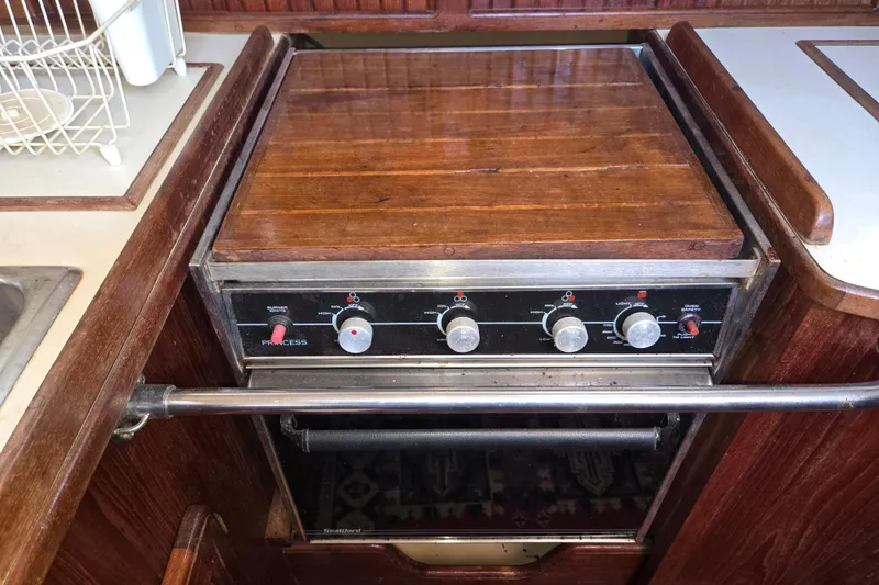 Slide: The Image of 1989 Island Packet 35 yacht kitchen with wooden stove cover and control knobs. - 43