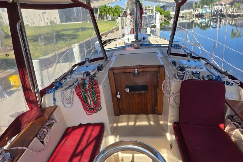 Slide: The Image of 1989 Island Packet 35 sailboat cockpit with red seating, ropes, and wooden hatch. - 5