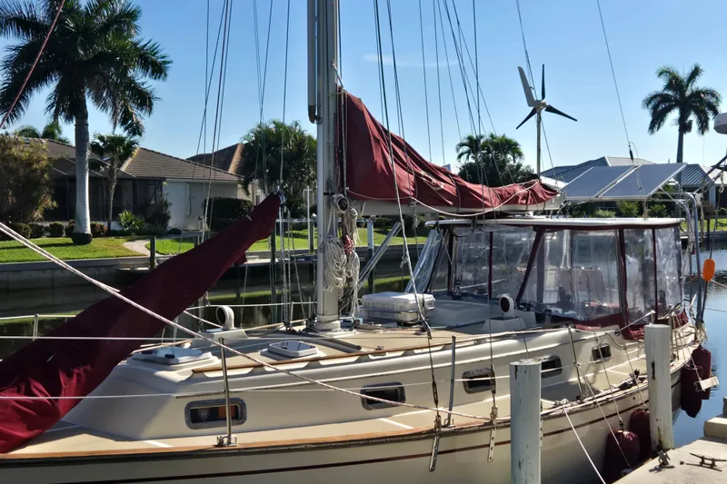 Slide: The Image of 1989 Island Packet 35 sailboat docked, featuring maroon sails and a clear canopy, surrounded by palm trees. - 56