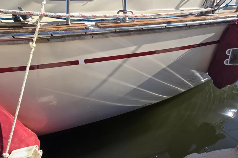 Slide: The Image of 1989 Island Packet 35 sailboat hull with red stripe and dockside reflections. - 69