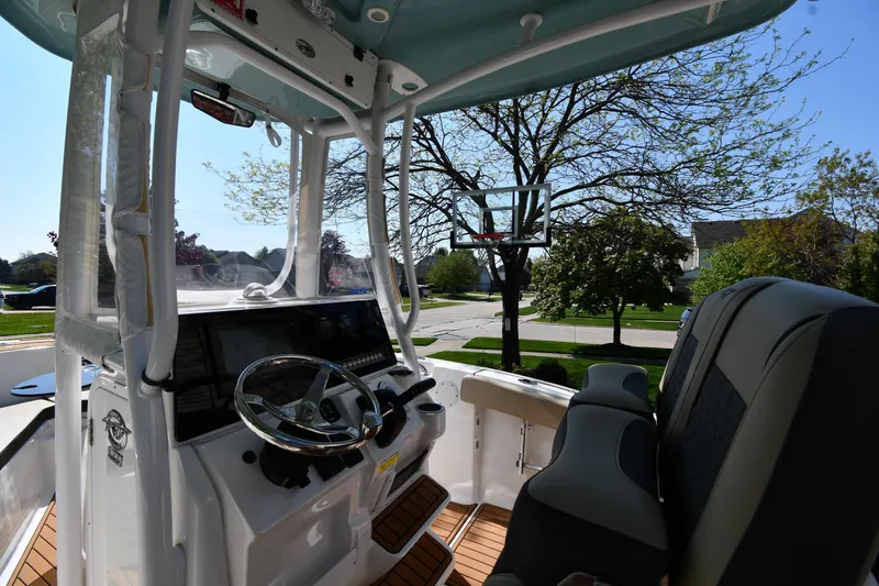 Slide: The Image of 2021 Tidewater 210 CC Adventure boat interior with steering wheel and seating, parked outdoors. - 10