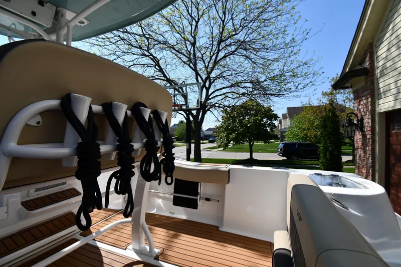 Slide: The Image of 2021 Tidewater 210 CC Adventure boat interior with rod holders and seating, parked in a suburban driveway. - 15