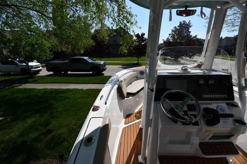 Slide: The Image of 2021 Tidewater 210 CC Adventure boat interior with steering wheel and dashboard, parked near trees. - 19