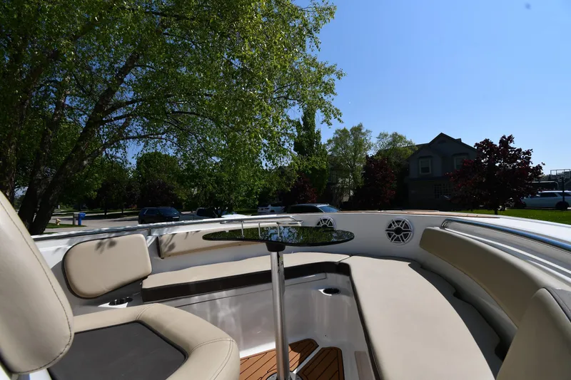 Slide: The Image of 2021 Tidewater 210 CC Adventure boat interior with seating and table, surrounded by trees. - 21