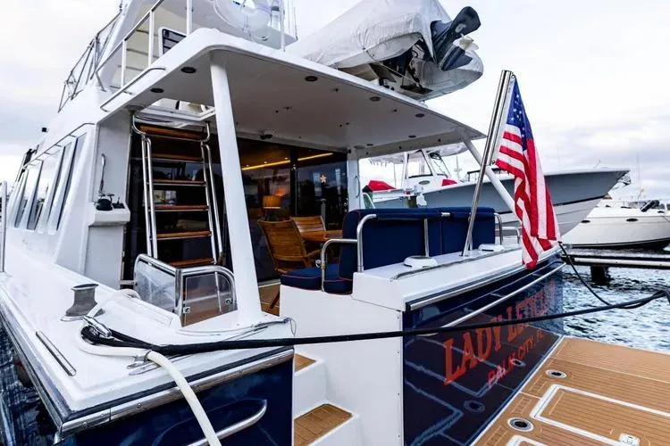 Slide: The Image of 2000 Pacific Mariner 65 Motoryacht docked, featuring American flag and elegant seating area. - 65