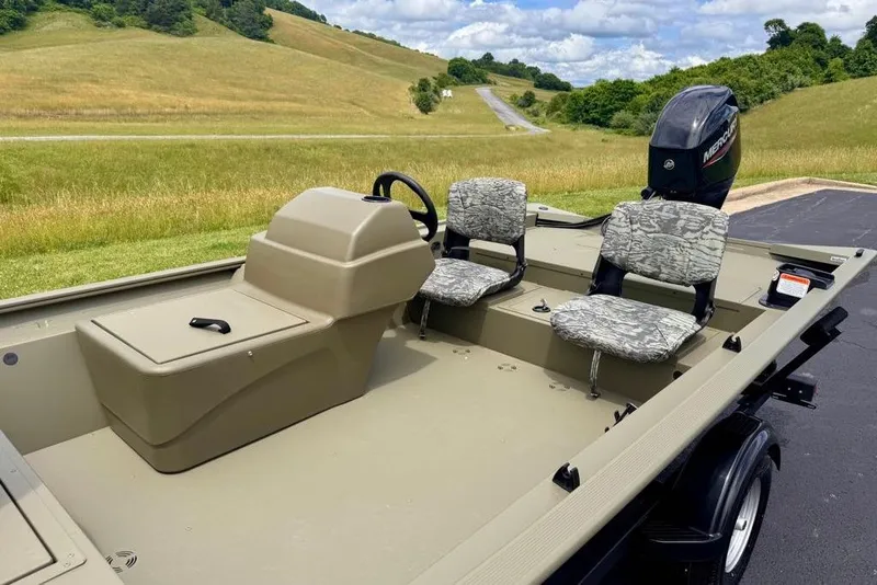 Slide: The Image of 2026 Tracker Grizzly 1754 SC boat with camo seats, parked on a scenic road. - 9